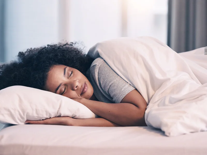 Jeune femme souriante exposée à la lumière naturelle du matin, symbolisant l'activation de l'horloge biologique.